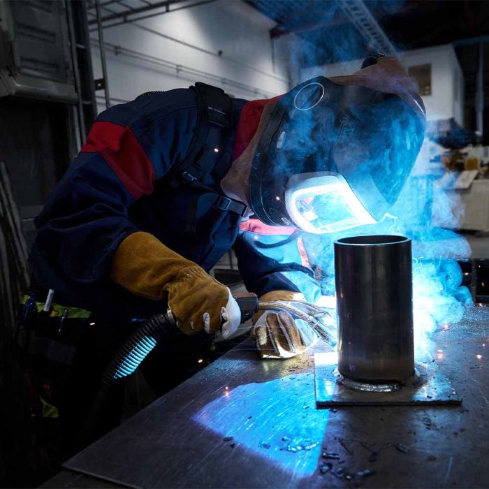 Person welding a metal object with protective gear in a workshop setting