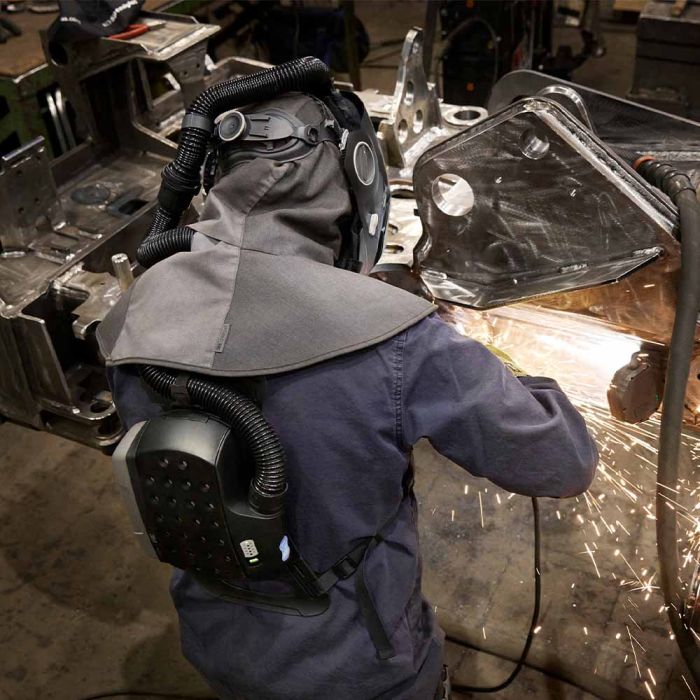 Back view of person wearing Speedglas G5-03VC Pro Air with Heavy-Duty Adflo PAPR welding helmet in a workshop with sparks flying.