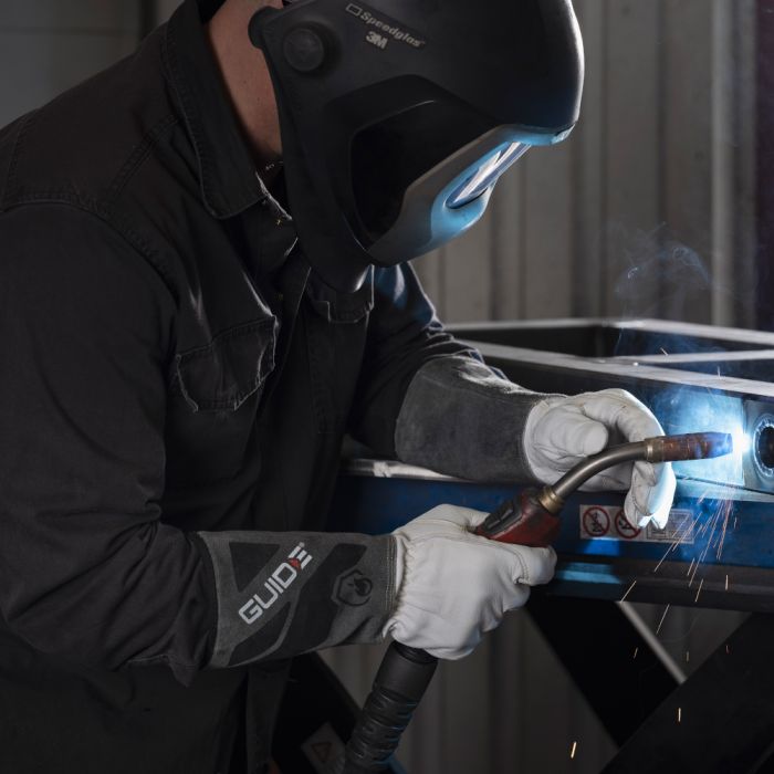 Person welding metal with protective gear on and wearing Guide 1270 in a workshop setting