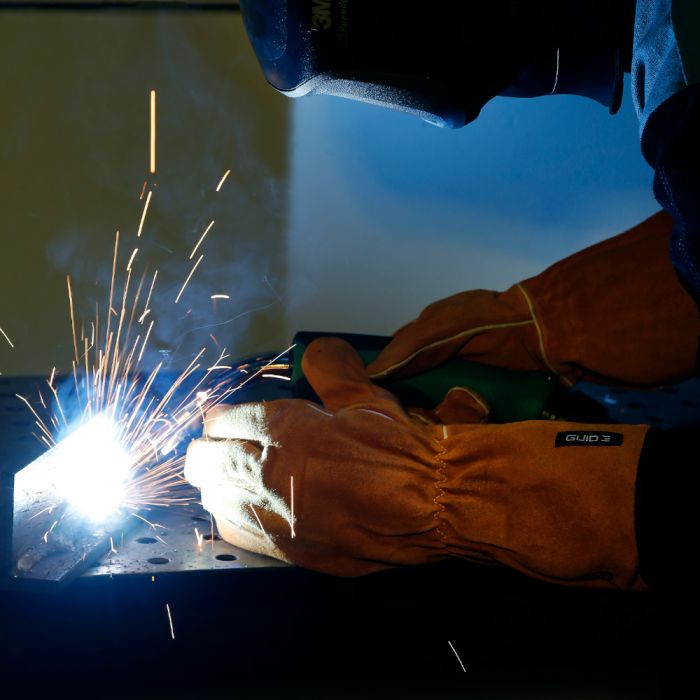 Person welding with sparks flying, wearing Guide 3569 protective gloves and a helmet.