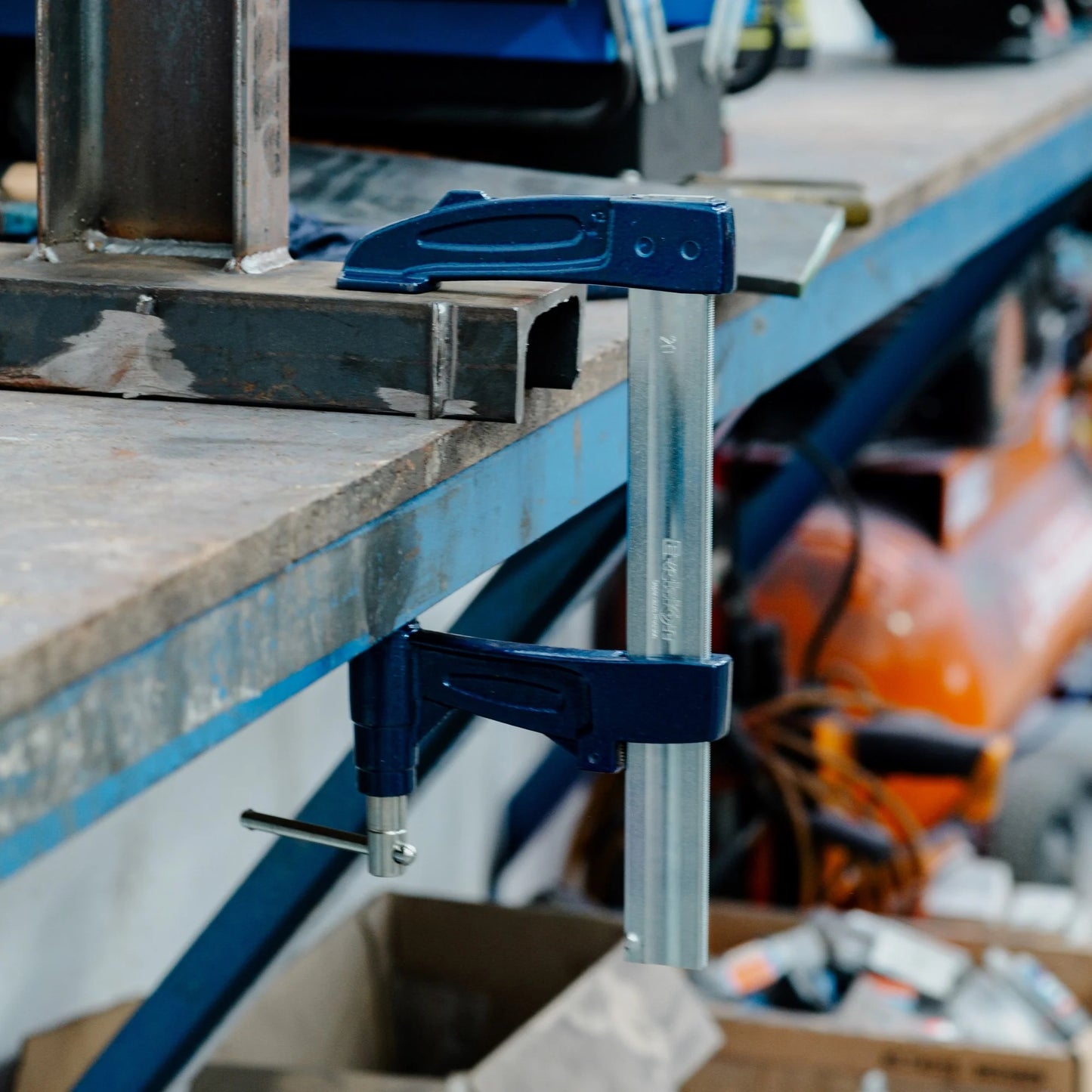 Blue Excision clamp on a metal workbench with tools in the background